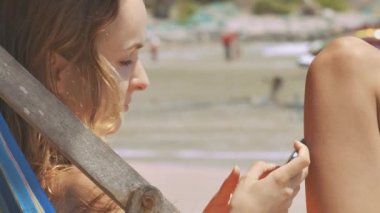 ahşap katlanır sandalye kum okyanus plaj ve telefon resimsel dalga sörf karşı metinlerde portre sarışın kız oturuyor