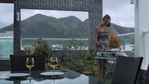 长马尾辫的女士在顶部屋顶露台烧烤肉由桌与酒杯反对大山 — 图库视频影像
