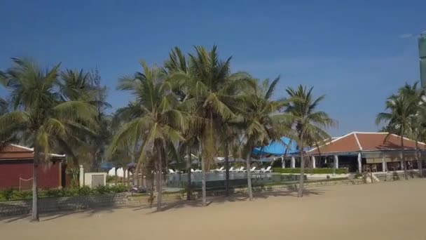 沿度假村海滩移动与棕榈树建筑和游泳池反对在无尽的蓝天下的酒店建设 — 图库视频影像
