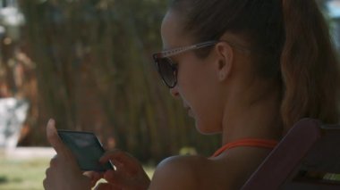 yakın yan görünümü kız güneş gözlüğü smartphone elinde tutan ve gölgeli bir yerde iletiyi okur