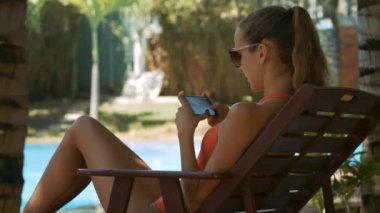 closeup arka görünümü kız at kuyruğu ile yanında Yüzme Havuzu koltuk katlama oturan smartphone ile arkadaş sohbetleri