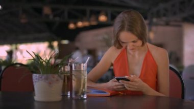 tatlı güzel kız smartphone kullanarak Internet sörf yapar ve bitki ve kokteyller kafede karşı masada oturur