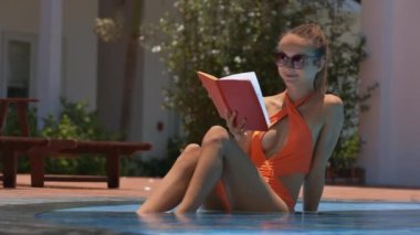 tatlı tatlı kız yüzme havuzunda oturuyor ve otel resort toprakları üzerinde ilginç bir kitap okur