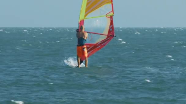 关闭背面视图秃头男子在橙色短裤 Windsurfs 冲浪板在广阔的暴风雨海洋 — 图库视频影像