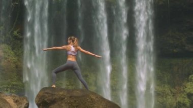 arka ışık üst ve tozluk teşkil yoga egzersiz yuvarlak kaya şelale karşı at kuyruğu ile sarışın kız göster