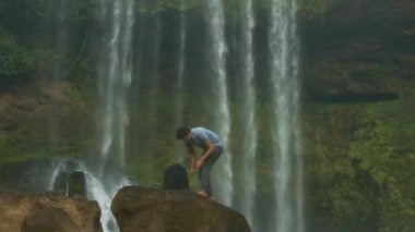 adam turist smartphone--dan sırt çantası ayakta büyük kayanın üzerinde alır ve fantastik şelale akarsu karşı selfie yapar