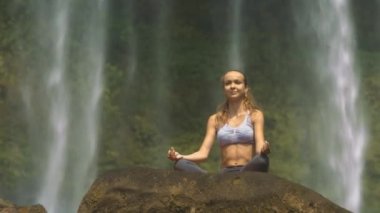 Görünümü güzel sarışın kız aşağıdan taş güzel şelale karşı nefes egzersiz yapar