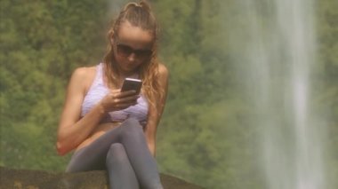 güneş gözlüğü uzun at kuyruğu closeup güzel sarışın kızla telefonunda büyük şelale karşı iletiyi okur