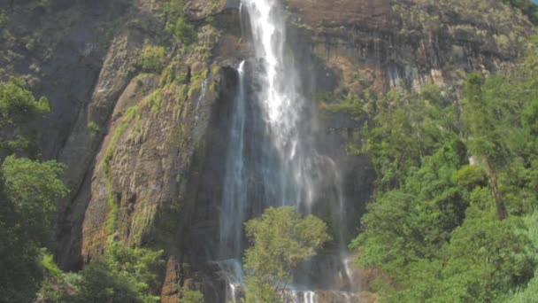 Мальовничий водоспад з високої кам'янистої скелі з зеленими деревами — стокове відео