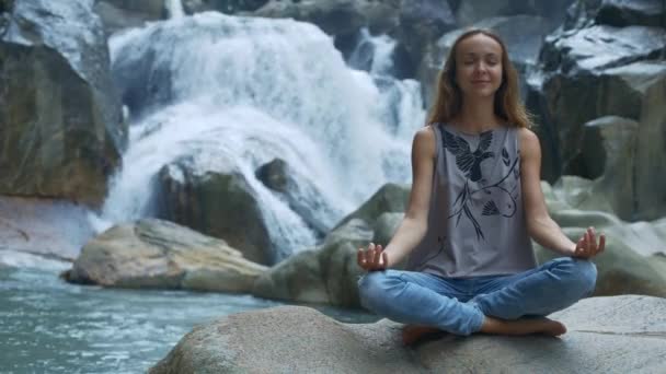 Flicka Sitter i Yoga Pose på stenar mot vattenfall — Stockvideo