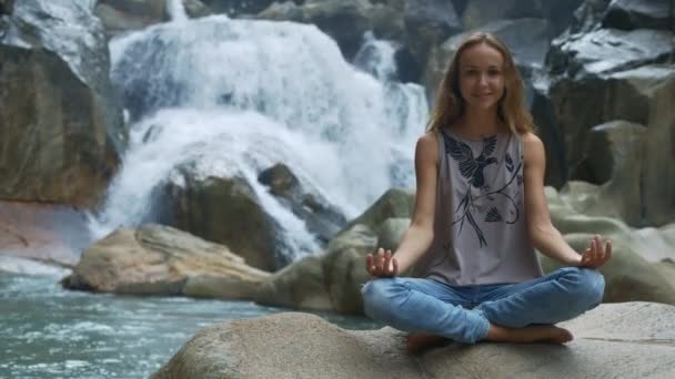 微笑的长毛女孩在瀑布附近做瑜伽吗？ — 图库视频影像