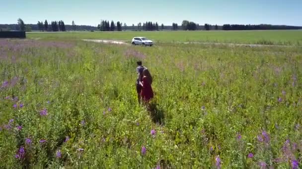 Casal se move para bom carro branco de pé perto do campo florescendo — Vídeo de Stock