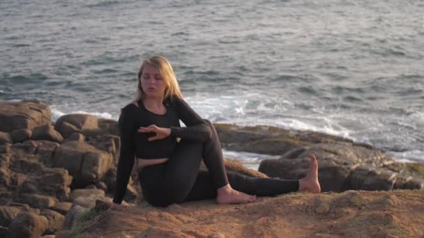 Pretty girl in black tracksuit sits on grey rocky cliff — Stock Video