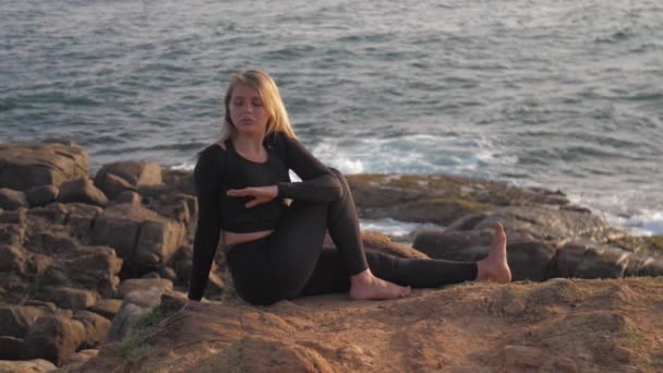 Pretty girl in black tracksuit sits on grey rocky cliff — Stock Video