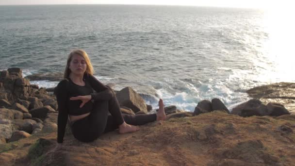 Pretty girl in black tracksuit sits on grey rocky cliff — Stock Video