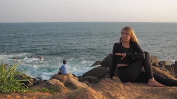 Pretty girl in black tracksuit sits on grey rocky cliff — 비디오