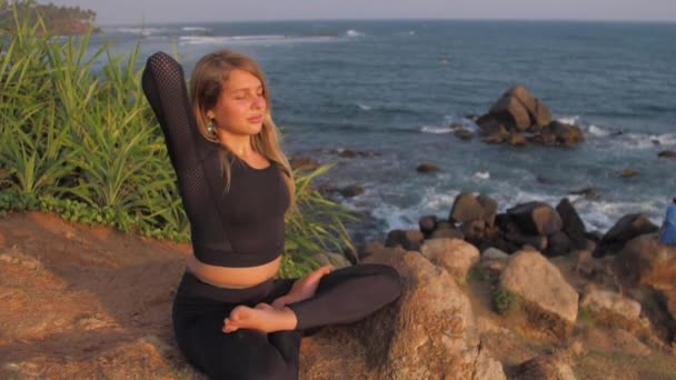Senhora em traje senta-se no penhasco em ioga pose contra o mar — Vídeo de Stock