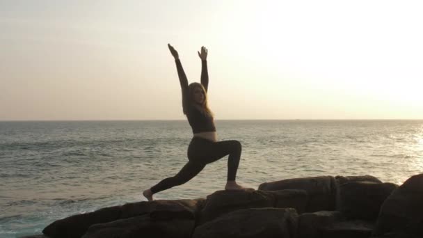 Girl silhouette practices yoga exercises standing on rock — Stock Video
