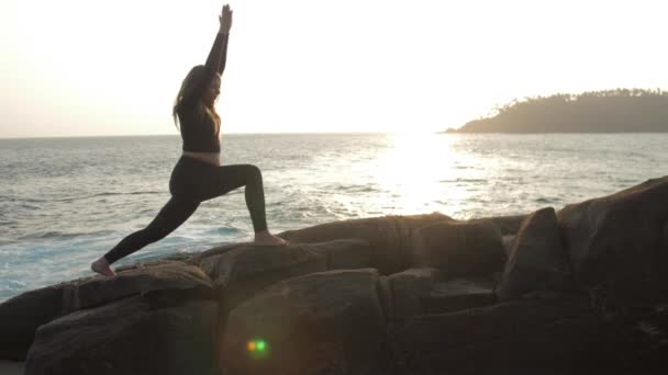 Girl silhouette practices yoga exercises standing on rock — 비디오