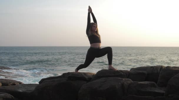 Young woman with long hair stretches on grey rocky cliff — Stock Video