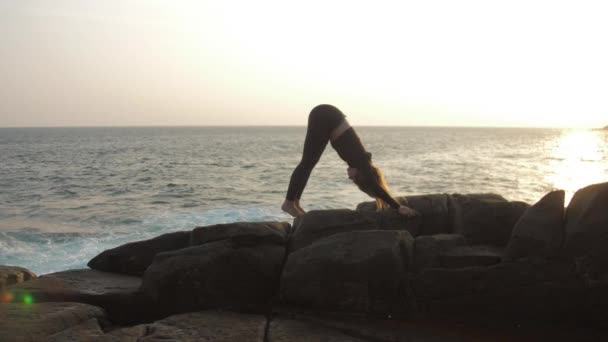 Dame im schwarzen Trainingsanzug steht in Yoga-Pose auf felsiger Klippe — Stockvideo