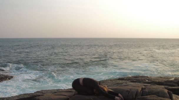 Jeune femme en survêtement noir s'étend sur une falaise rocheuse grise — Video