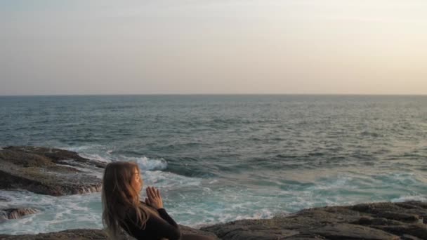 Jeune femme en survêtement noir s'étend sur une falaise rocheuse grise — Video