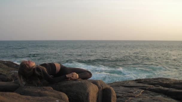 Young woman in black tracksuit stretches on grey rocky cliff — Stock Video