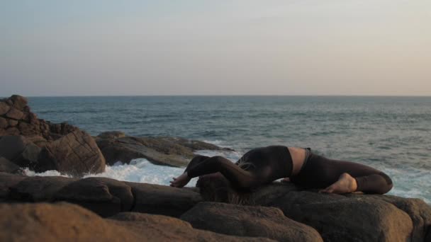 Young woman in black tracksuit stretches on grey rocky cliff — Stock Video