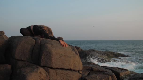 Young woman in black tracksuit stretches on grey rocky cliff — 비디오