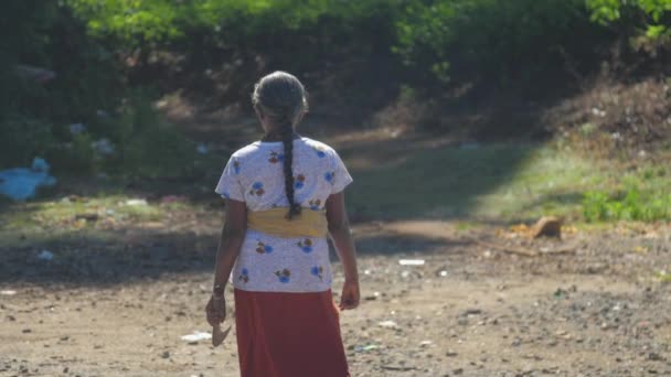 senior femme en jupe avec machette promenades le long de la route sale 