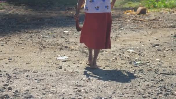 Старша жінка в спідниці з мачете ходить по брудній дорозі — стокове відео