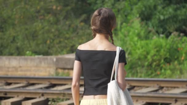 Дівчина в чорному топ ходить залізницею серед природи повільний рух — стокове відео