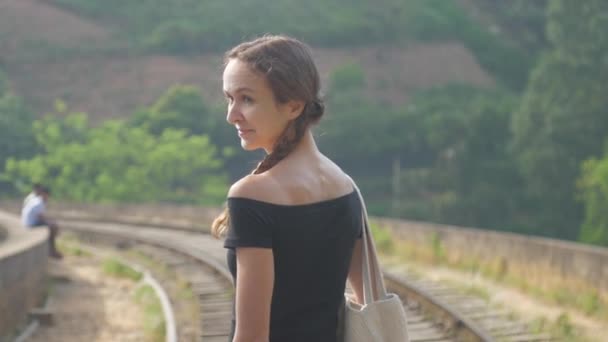 Fille en noir top promenades à vieux chemin de fer parmi jungle souriant — Video
