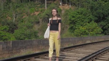 girl tourist walks on old railway track among jungle smiling
