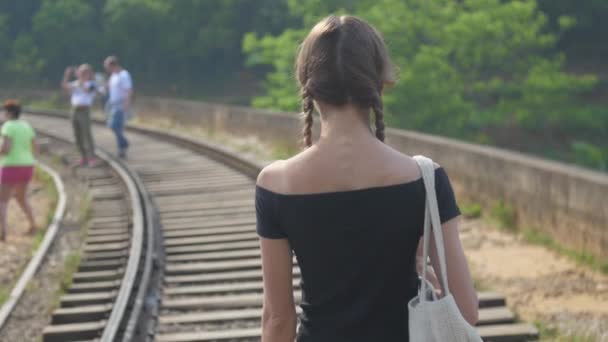 Girl walks along track on bridge to tourists taking photos — ストック動画