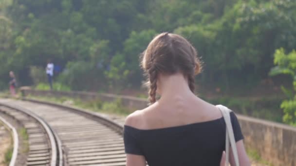 Girl in black top walks on old railway trail among jungle — ストック動画