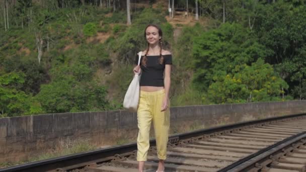 Dívka turistické procházky na staré železniční trati mezi džunglí s úsměvem — Stock video