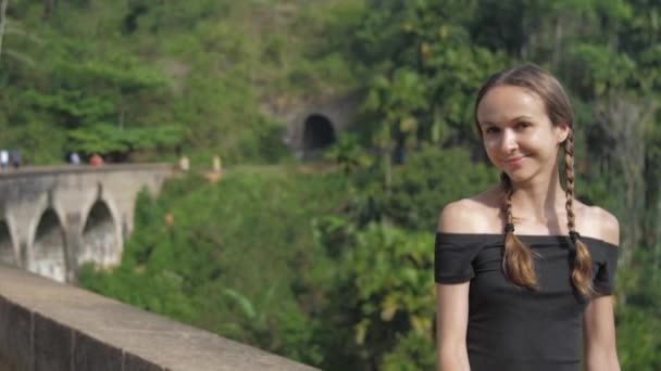 Menina bonita senta-se na ponte de nove arcos entre a natureza verde — Vídeo de Stock