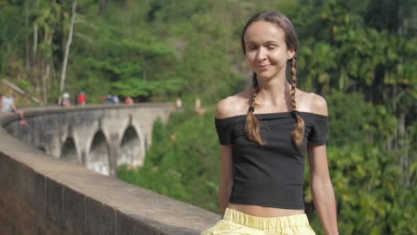 Menina senta-se na barreira ponte e goza de natureza tropical selvagem — Vídeo de Stock