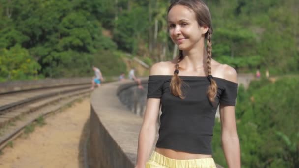 Girl sits on bridge barrier and smiles at tropical nature — ストック動画