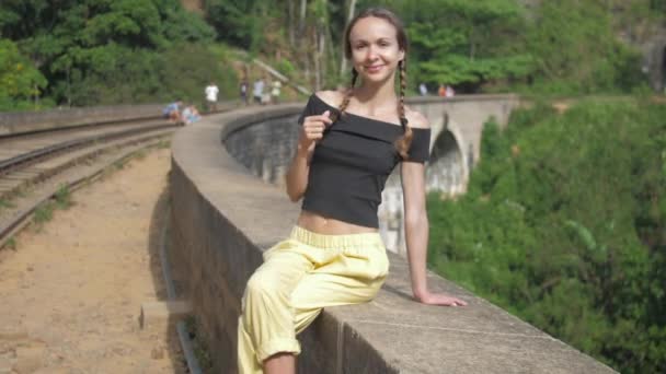 Muchacha trenzas poses en viejo puente sonriendo contra bosque — Vídeo de stock