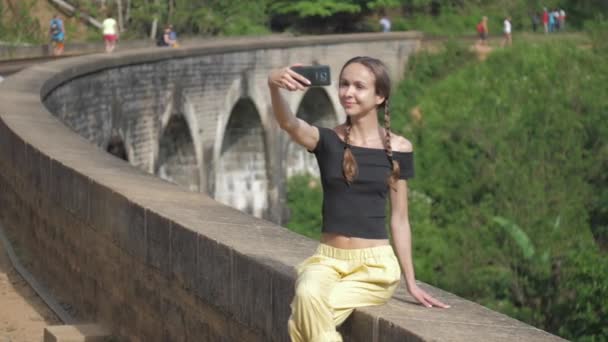 Nettes Mädchen mit Zöpfen macht Selfie auf alter Brückenbarriere — Stockvideo