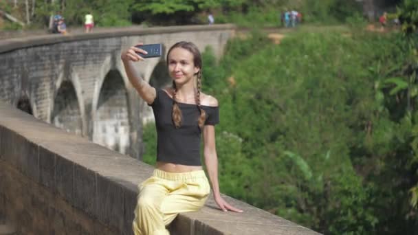 Ωραίο κορίτσι με μαύρο μπλουζάκι κάνει selfie στο παλιό εμπόδιο γέφυρα — Αρχείο Βίντεο