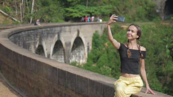 Chica en negro top hace selfie sentado en puente barrera — Vídeos de Stock