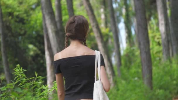 Молодая женщина бродит по зеленому лесу с белой сумкой — стоковое видео