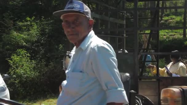 Мужчина сидит на маленьком тракторе с прицепом и женской весовой сумкой — стоковое видео