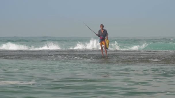 Pescador camina a lo largo de borde de surf de agua en olas marinas espumosas — Vídeos de Stock