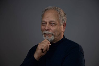 Gri stüdyo geçmişi olan düşünceli yaşlı bir adam.