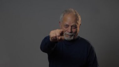 Gri stüdyo arka planında parmağı olan yaşlı adam.